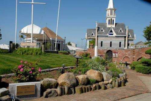 A scenic view of a park with a church-like building, flowers, and a sign for parking and bridal interviews.