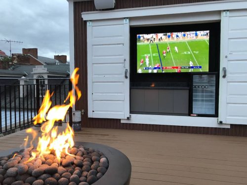 A cozy outdoor space featuring a fire pit and a TV displaying a football game.