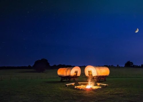 Two illuminated wagons near a campfire under a starry night sky, with a crescent moon visible.