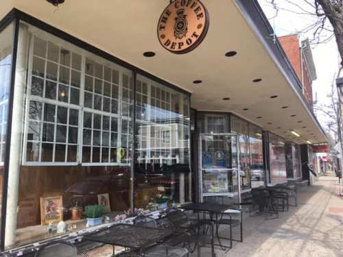 Exterior view of a coffee shop with large windows, outdoor seating, and a sign reading "The Coffee Depot."