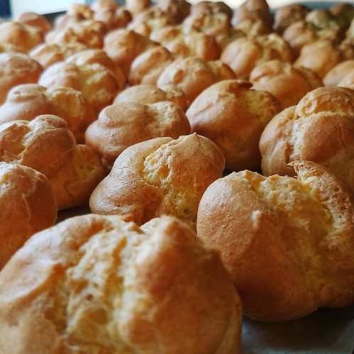 A close-up of freshly baked golden cream puffs arranged in rows on a tray.
