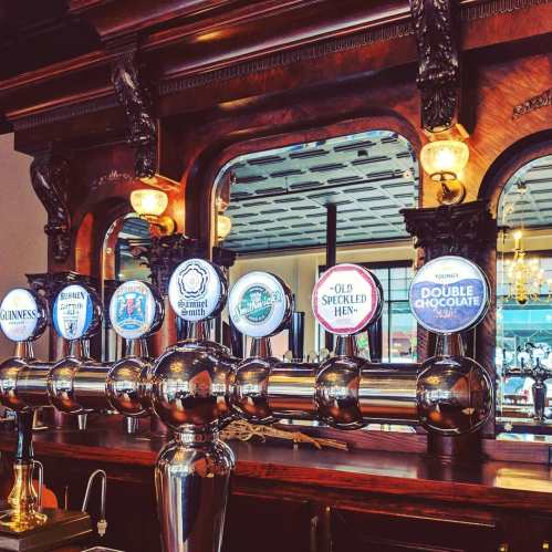 A polished bar with various beer taps and a vintage wooden backdrop, reflecting warm light from overhead fixtures.