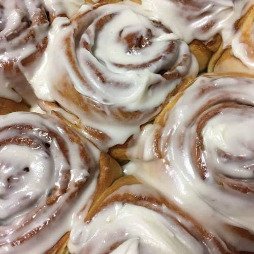 Close-up of freshly baked cinnamon rolls topped with creamy white icing, showcasing their swirled layers.