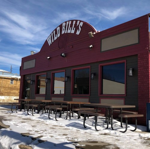 Exterior of Wild Bill's restaurant with a red and brown facade, large windows, and outdoor seating on a snowy day.