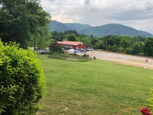 A scenic view of a red barn surrounded by green trees and mountains, with people gathered outside on a cloudy day.