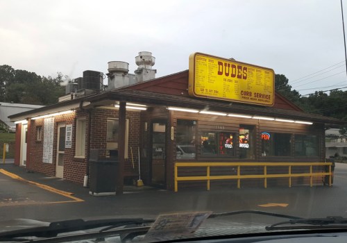 A small, retro-style fast food restaurant with a yellow sign displaying the menu and curb service.