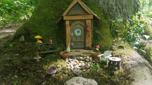 A whimsical fairy house nestled at the base of a tree, surrounded by miniature decorations and colorful mushrooms.