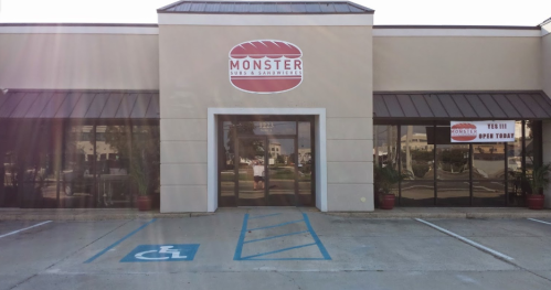 Exterior of a sandwich shop named "Monster Subs & Sandwiches," featuring a large sign and accessible parking.