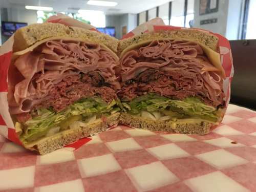 A large sandwich cut in half, filled with layers of deli meats, cheese, and lettuce on multigrain bread.