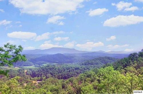 A scenic view of rolling green hills and mountains under a bright blue sky with fluffy white clouds.