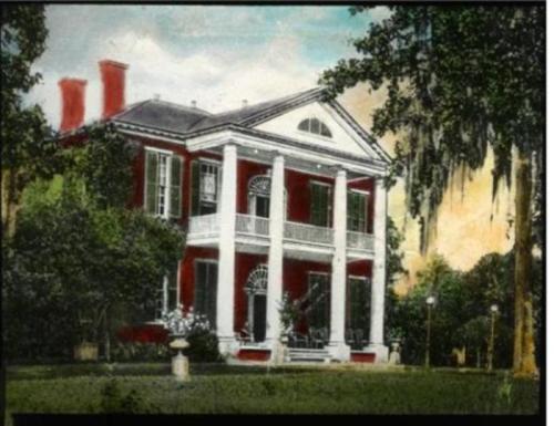 A historic red mansion with white columns, surrounded by lush greenery and trees, under a colorful sky.