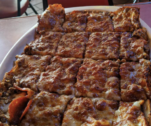 A close-up of a rectangular pizza with a crispy crust, topped with melted cheese and pepperoni, cut into squares.