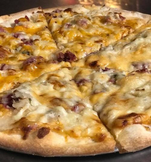 A close-up of a sliced pizza topped with melted cheese and bits of meat, served on a dark surface.