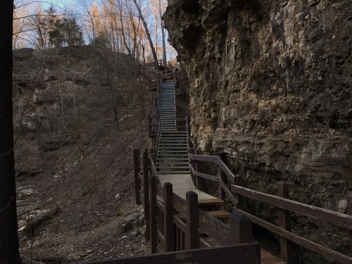 A wooden staircase leads up a rocky hillside, surrounded by trees and rugged terrain.