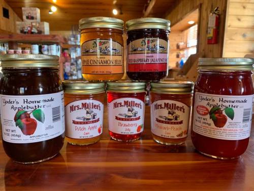 A variety of jars filled with different fruit preserves and apple butter, displayed on a wooden table.