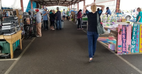 A bustling market scene with vendors and shoppers under a covered area, colorful displays on both sides.
