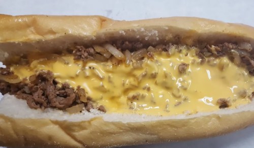 A close-up of a sandwich filled with ground beef, melted cheese, and sautéed onions in a soft hoagie roll.