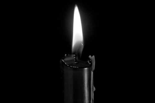 A single candle flame flickers against a dark background, casting a warm glow.