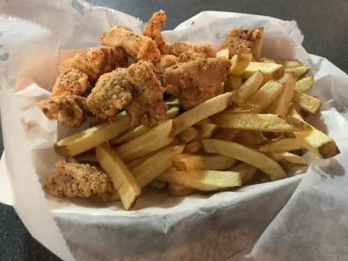 A basket of crispy fried chicken pieces served with golden French fries.