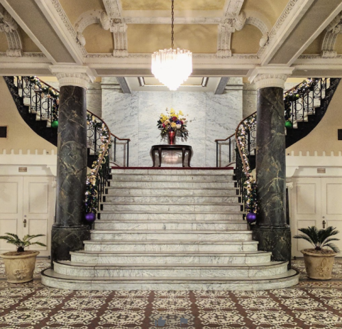 Elegant staircase with marble steps, ornate railings, and a chandelier, adorned with flowers and decorative elements.