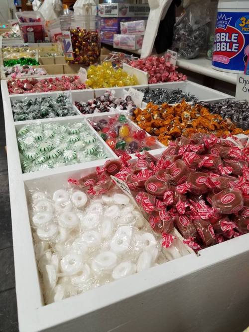 A variety of colorful candies displayed in white bins, including wrapped sweets and gummies.