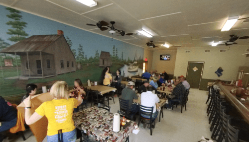 A cozy restaurant interior with diners at tables, featuring a mural of a rural landscape on the wall.