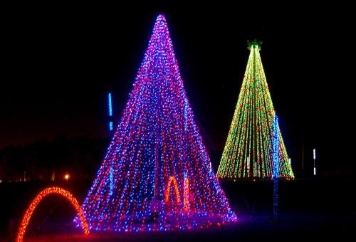 Two large, brightly lit Christmas trees made of colorful lights, set against a dark night sky.