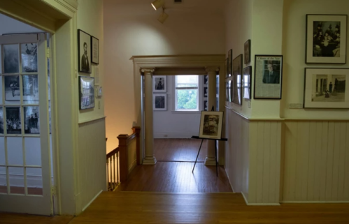 A hallway with wooden floors, framed photos on the walls, and a display stand in the center.