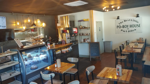 Cozy interior of a po-boy restaurant with wooden tables, a display fridge, and a welcoming sign on the wall.