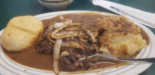 A plate of meatloaf topped with onions, served with mashed potatoes and a side of cornbread.
