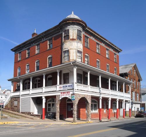 Historic red brick building with a rounded corner, featuring a porch and multiple stories under a clear blue sky.