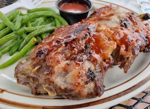 A plate featuring two pieces of glazed meat with a side of green beans and a small cup of sauce.