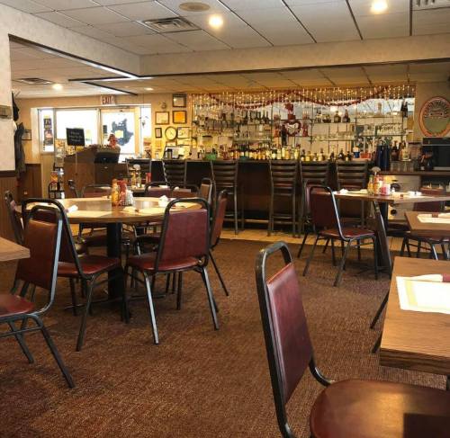 Cozy restaurant interior with empty tables, a bar in the background, and decor on the walls.