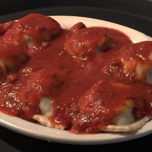 A plate of ravioli topped with rich tomato sauce, served on a black background.