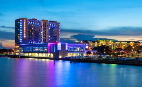 A vibrant waterfront scene featuring a modern building illuminated with colorful lights at dusk.