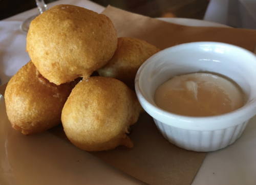 A stack of golden, fried dough balls served with a small bowl of creamy dipping sauce.