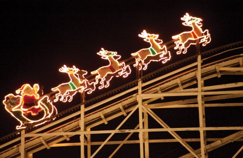 Colorful Christmas lights depict Santa and reindeer on a roller coaster at night.