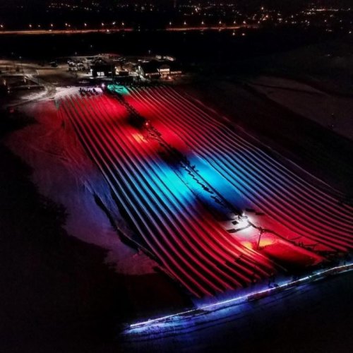Aerial view of illuminated fields with colorful lights creating patterns against a dark landscape.