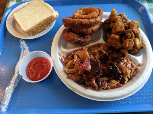 A blue tray with a plate of pulled pork, onion rings, fried okra, a slice of bread, and a cup of ketchup.
