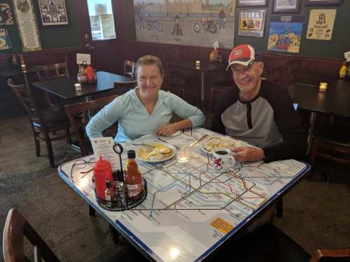 A man and woman sit at a table with a subway map design, enjoying breakfast in a cozy restaurant.