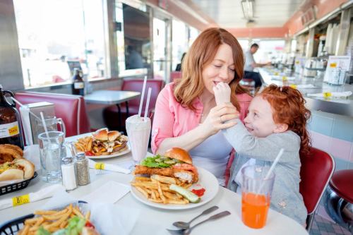 A woman and a young girl share a joyful moment at a diner, surrounded by plates of food and drinks.
