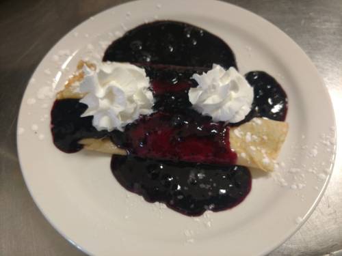 A plate with crepes topped with blueberry sauce and whipped cream, resembling a playful face.