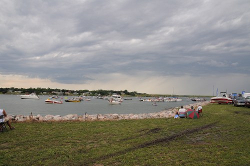 A cloudy sky over a river with boats and people sitting on the shore, enjoying a recreational day outdoors.