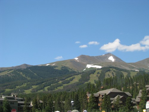 Scenic view of mountains with green slopes and patches of snow under a clear blue sky.