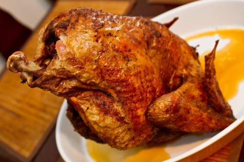 A golden-brown roasted turkey on a white platter, with a small pool of orange sauce underneath.