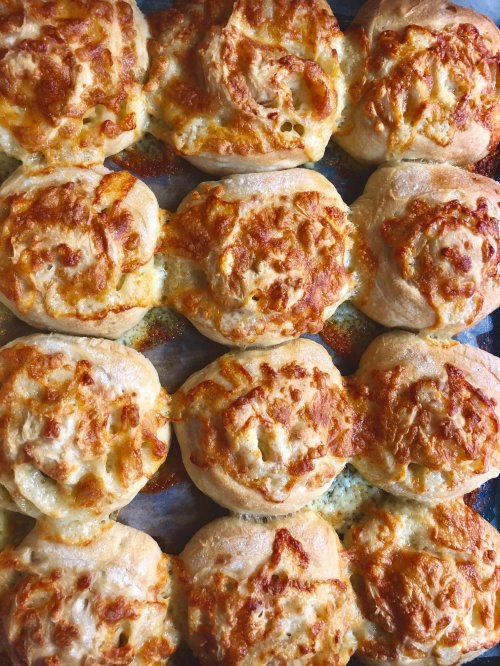 Golden, cheesy rolls arranged in a tray, with a crispy, melted cheese topping and soft, fluffy bread underneath.