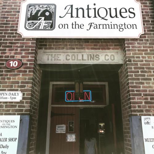 Sign for "Antiques on the Farmington" with a neon "OPEN" sign and brick facade.