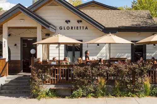 A cozy restaurant named Glorietta with outdoor seating and umbrellas, surrounded by greenery and patrons enjoying their meals.