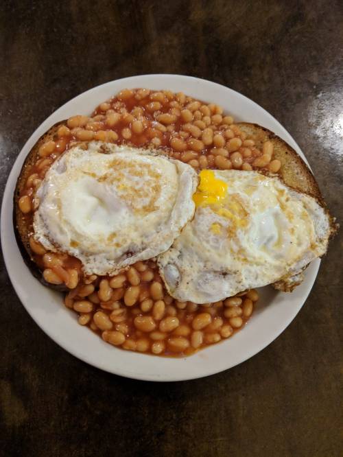 A plate with baked beans and two fried eggs on toasted bread.
