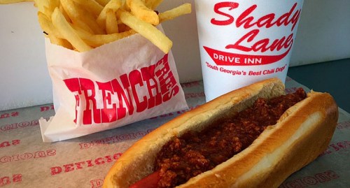 A chili dog with fries and a drink from Shady Lane Drive Inn on a paper-lined table.